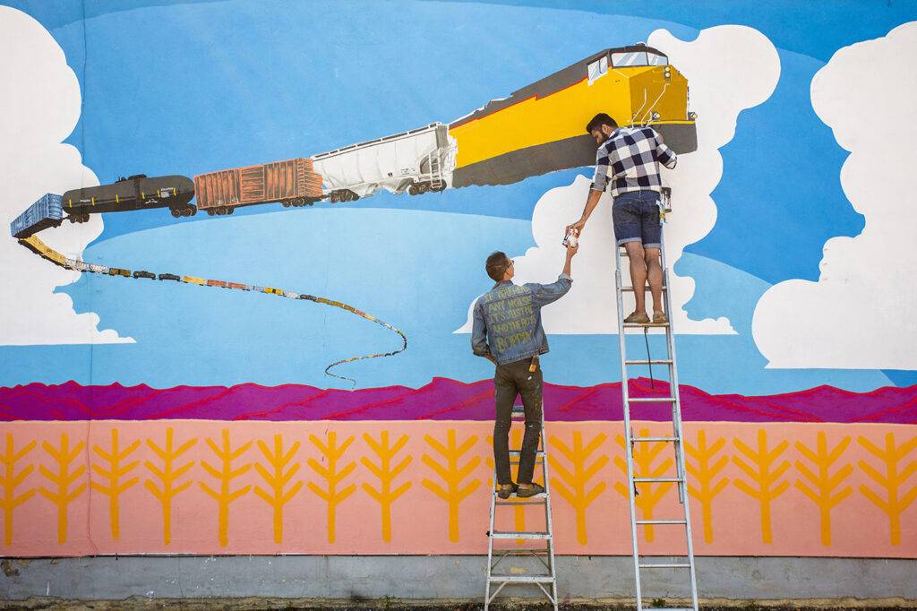 Artists Creating A Train Mural On The Side Of A Building