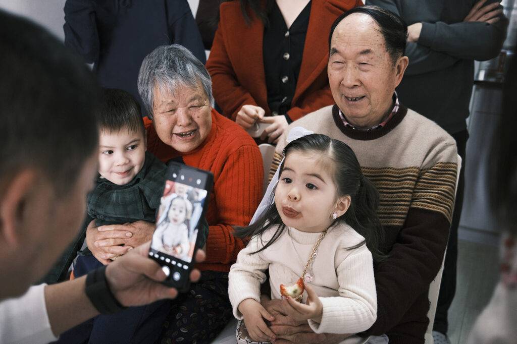 An East Asian man takes a group portrait with his cell phone of his smiling extended family during Chinese New Year.
