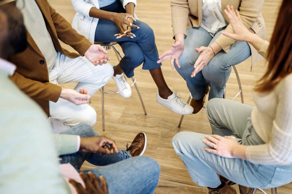 High angle of crop anonymous multiracial male and female employees in smart casual outfits sitting on chairs and discussing new business strategy during team building in modern office. Communication concept