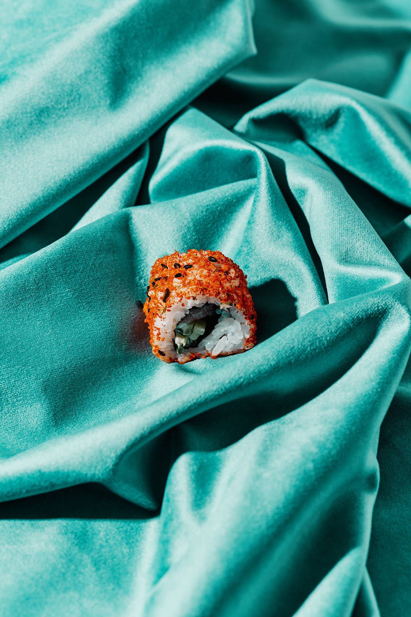 a piece of sushi on a draped greenish blue fabric