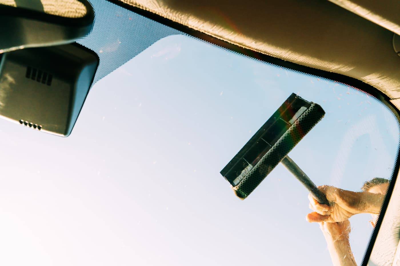 A vehicle going through a car wash. The windshield being washed with a sponge by hand. An unidentified person is holding the tool.