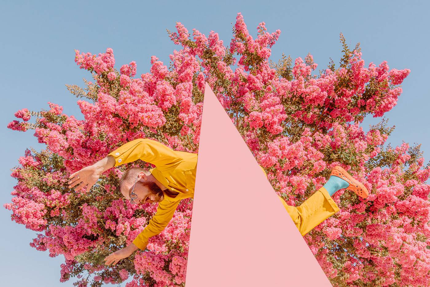 Man in yellow jumpsuit poses in front of pink blossoming tree