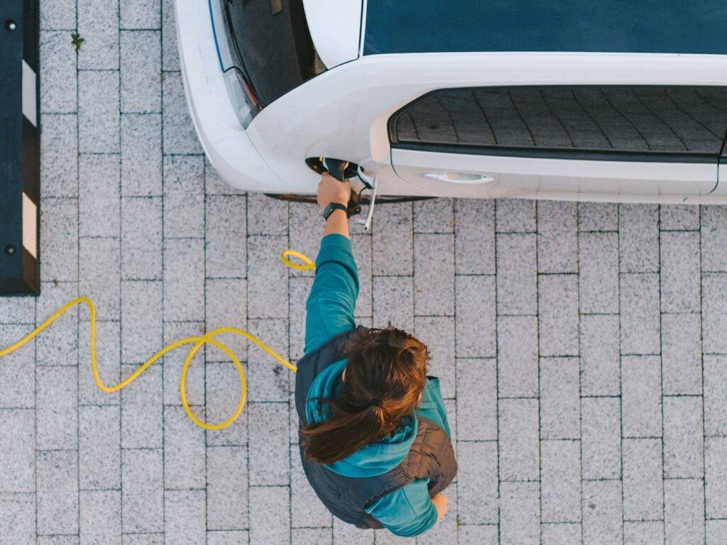Girl charging electric car. Drone aerial view. Top down perpective