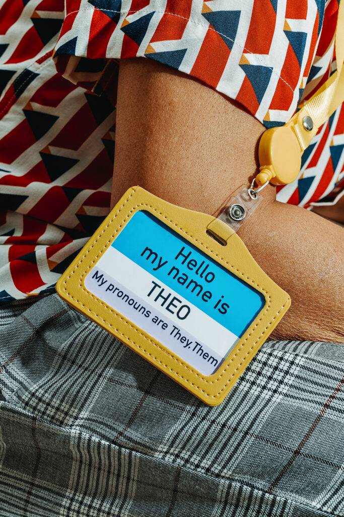 a person wears a tag with the text Hello my name is Theo, my pronouns are they, them