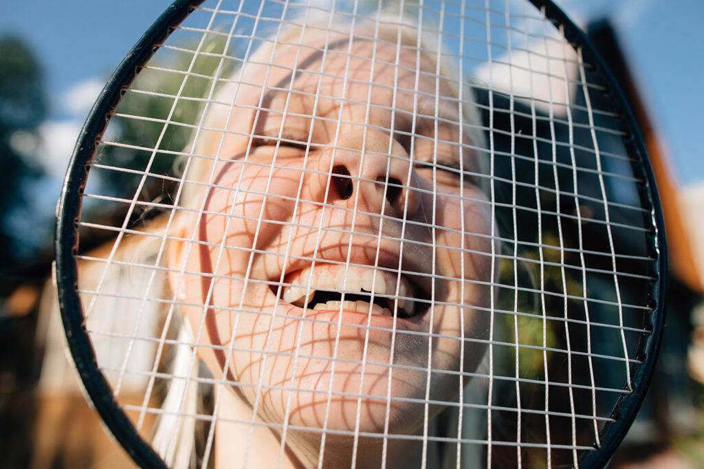 Smiling Face Through The Badminton Racquet Laughing blond teen girl puts a racket on her face outdoors