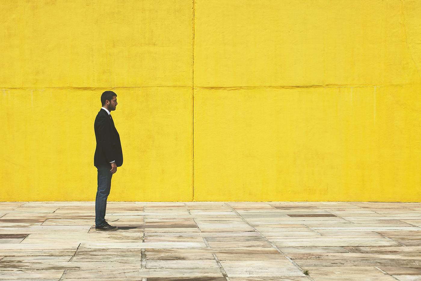 Businessman walking on the street in front a yellow big wall.