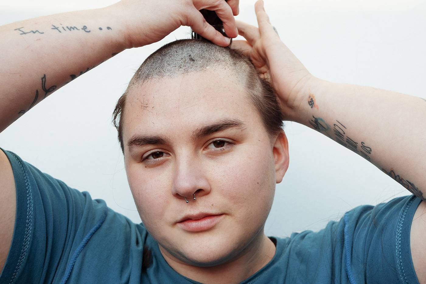 Non-binary person shaving his head against a white wall. Haircut Concept. Lgbt+ Concept