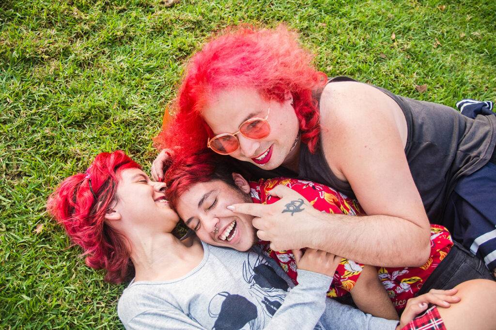 Three latino transgender friends are lying in the grass in a park hugging each other lovingly and having fun. LGBTQ friendship and community.https://www.stocksy.com/analuzcrespi