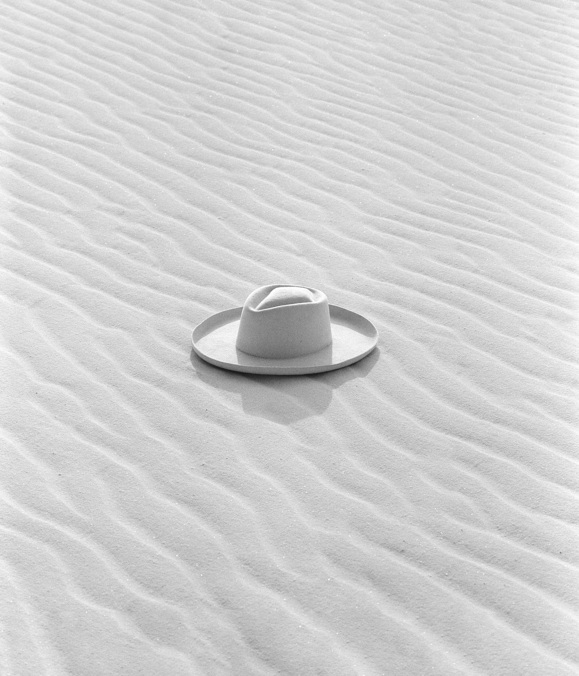 White cowboy hat sitting in wavy sand in the desert.