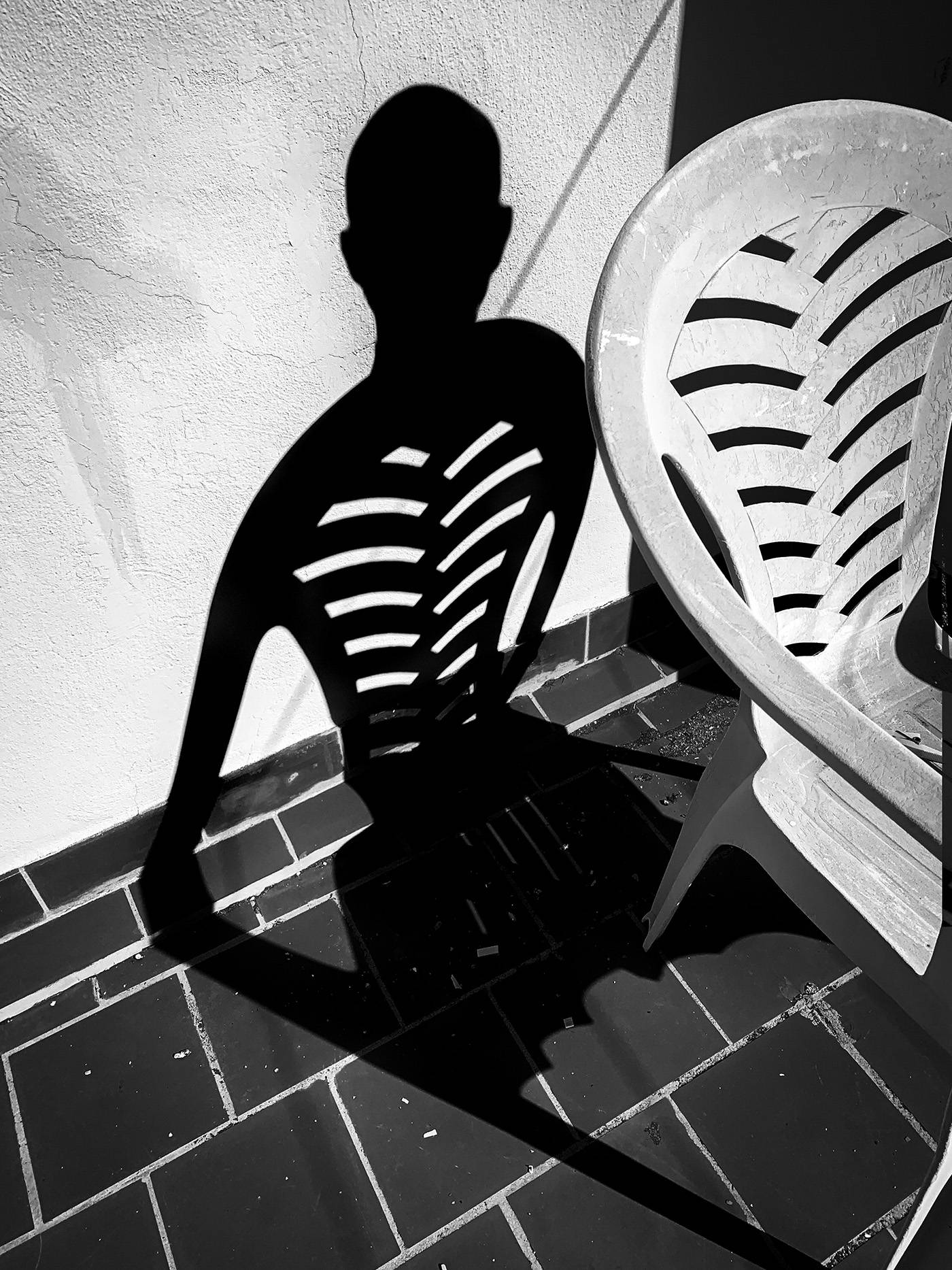 Shadow of a man with the form of an alien with his ribs visible thanks to a chair.