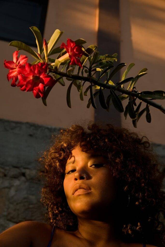portrait of a curly-haired woman among magenta flowers with sunset light