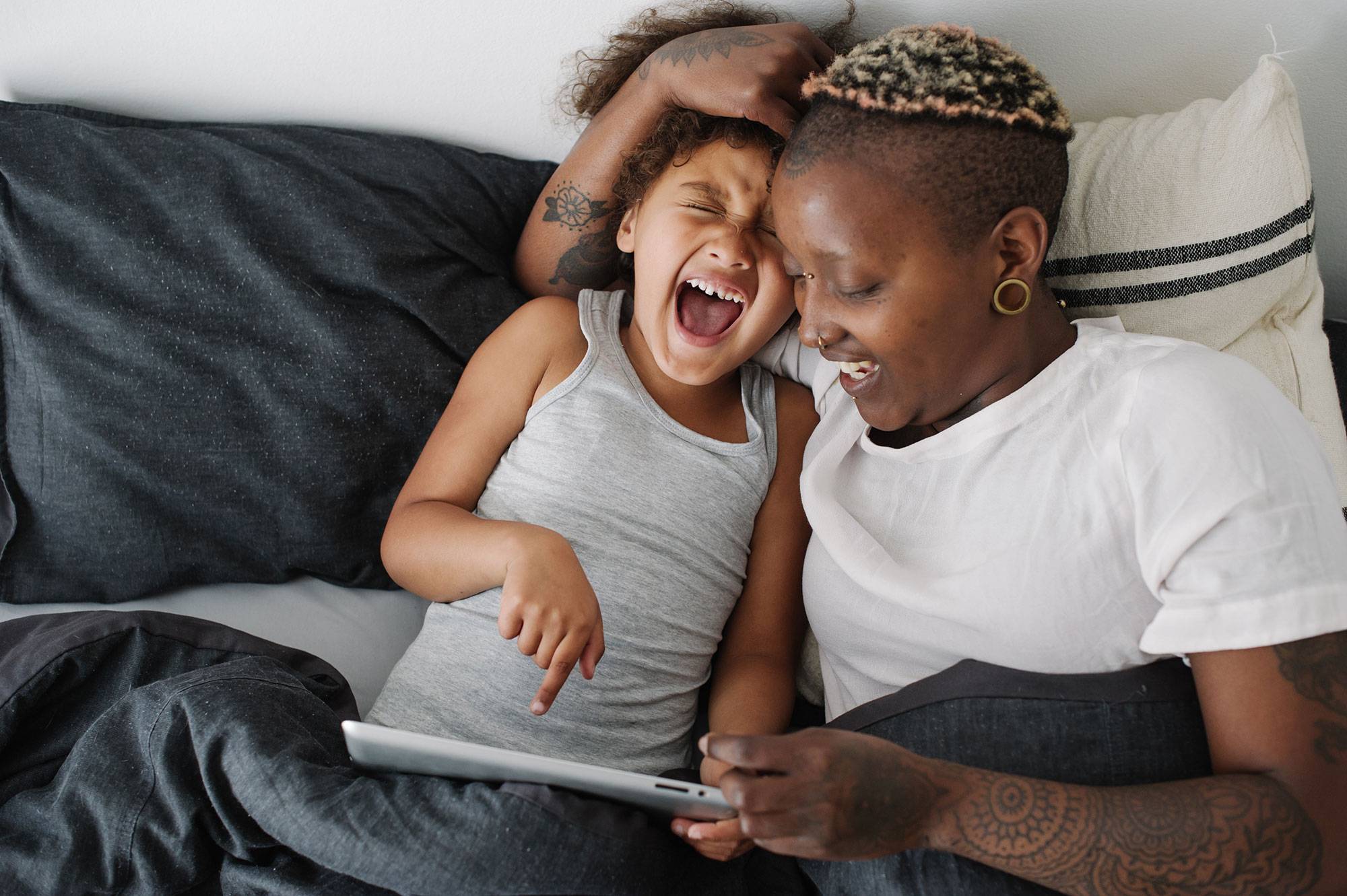 A mother and her daughter read stories on a tablet before bed