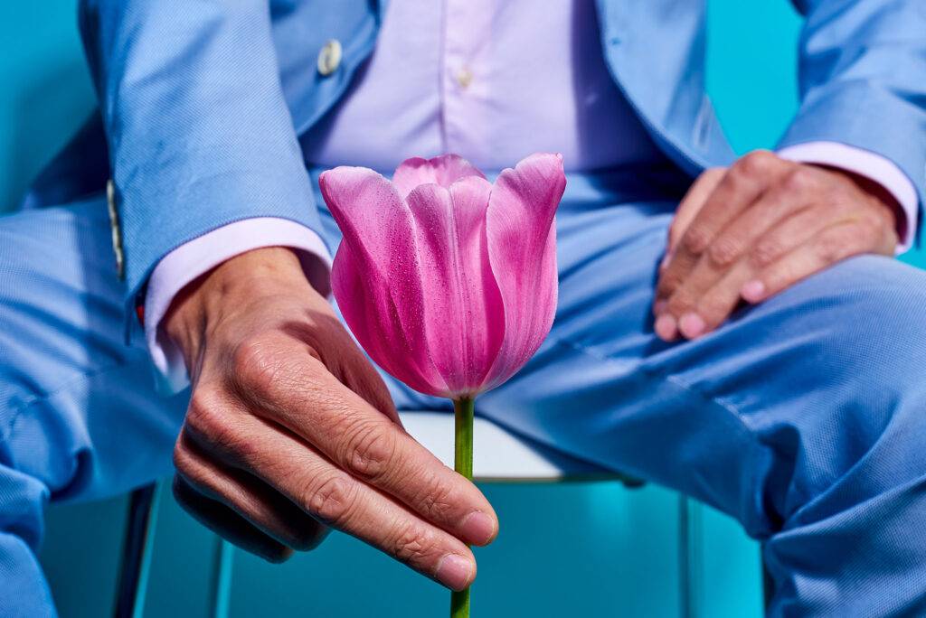 man in a blue suit holding a pink tulip in front of him