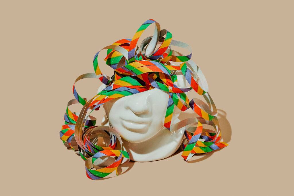 closeup of a cut off porcelain head and some multicolored streamers peeping out of it, on a beige background