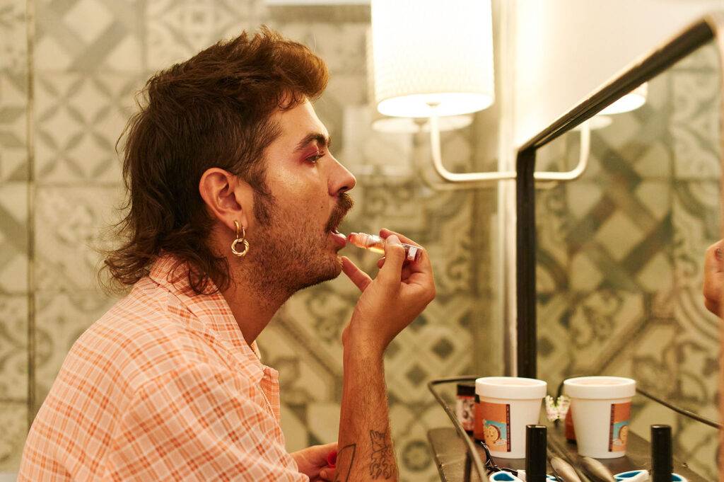 Young gay man putting on lip gloss his bathroom mirror at home before going out
