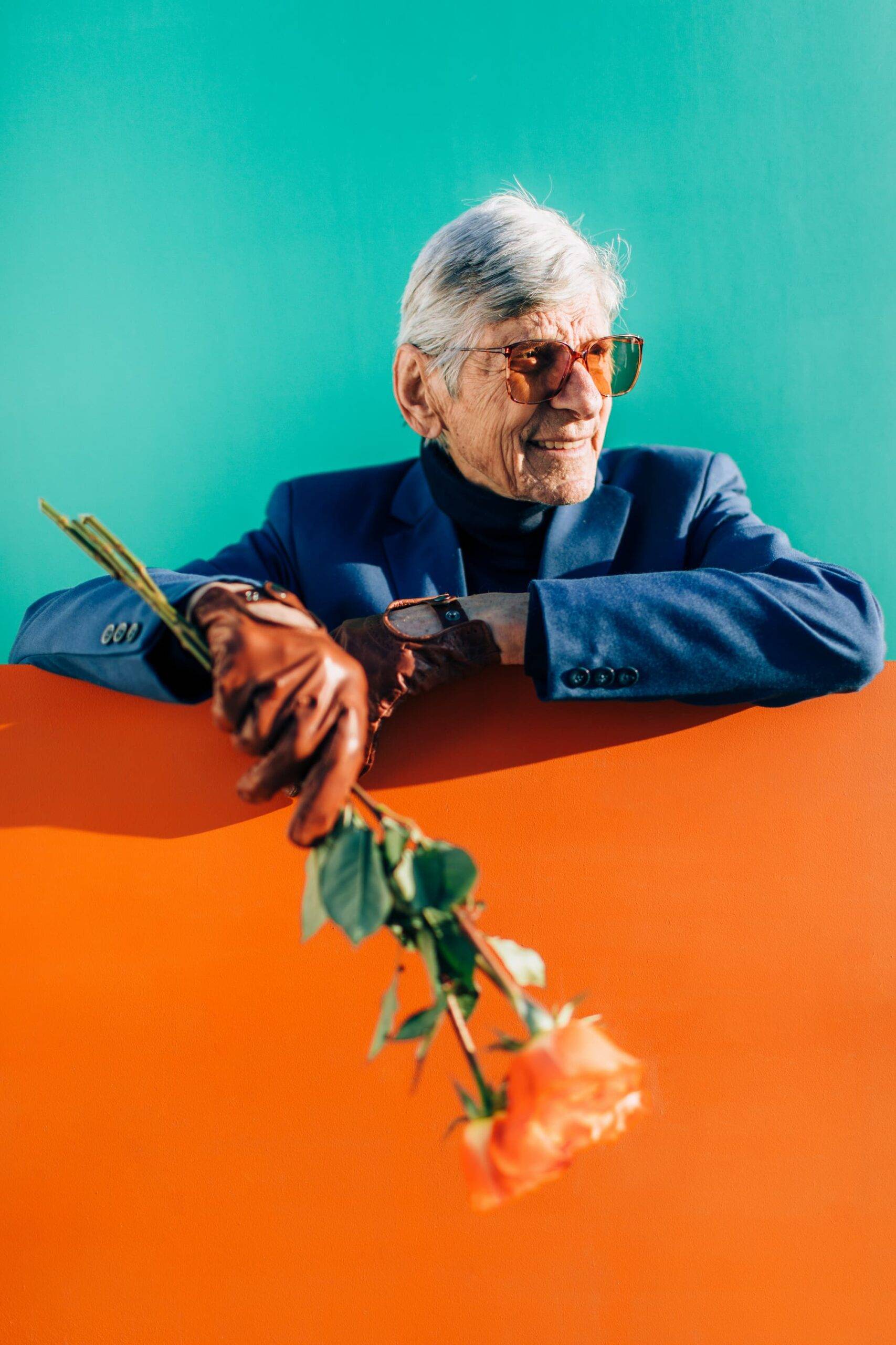 Senior modern Grandpa, holding a bouquet of roses in front of a orange-green background.