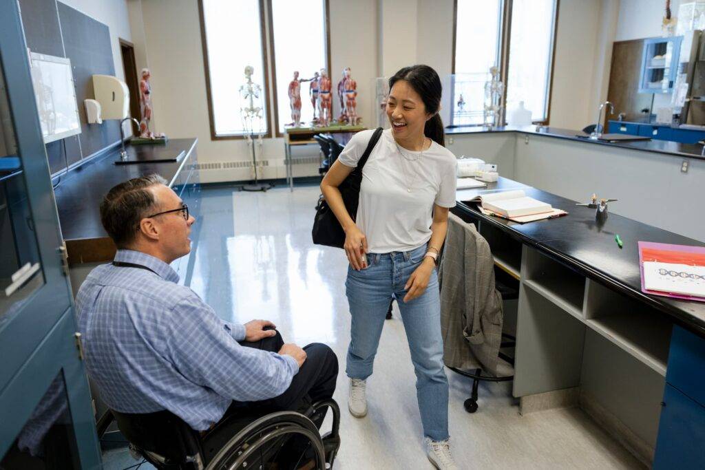 College Student Talking With Science Professor In Wheelchair In Lab.