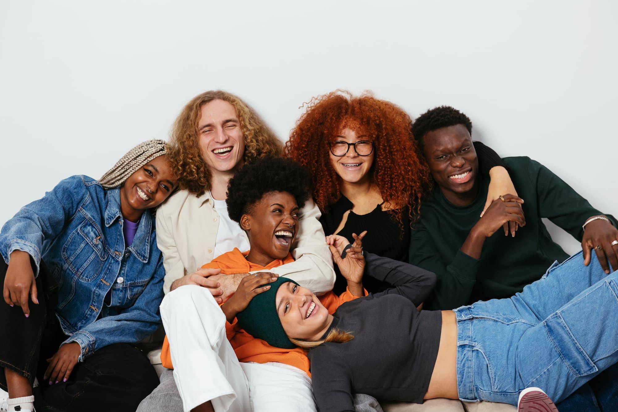 Group of cheerful teenage friends in stylish clothes embracing and looking at camera while sitting on floor in studio