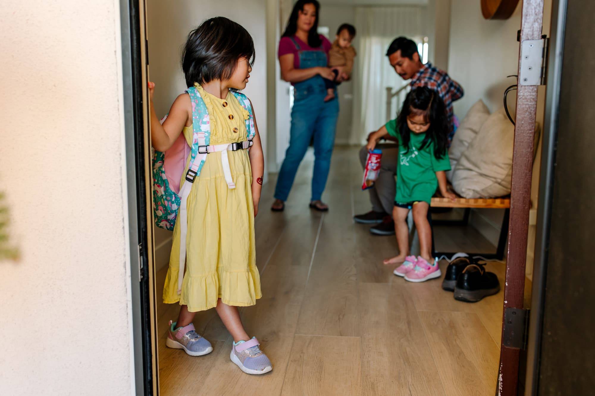 Cute family with mom, dad, and three children getting ready in the morning to go to school. It is summer and the daughters are wearing both a dress and a short sleeve shirt with shorts.