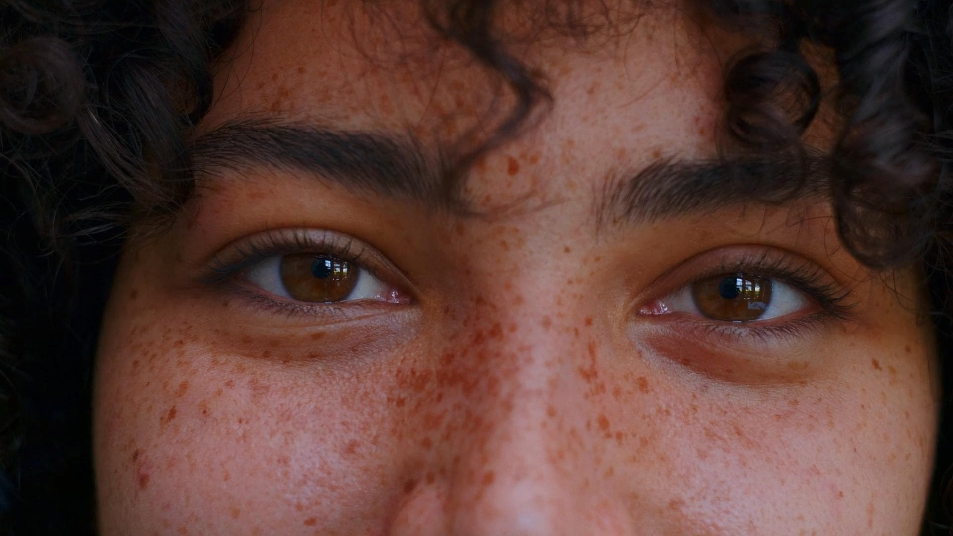An extreme close up portrait of a beautiful mixed race woman with freckles and a big curly afro smiling and tilting her head.