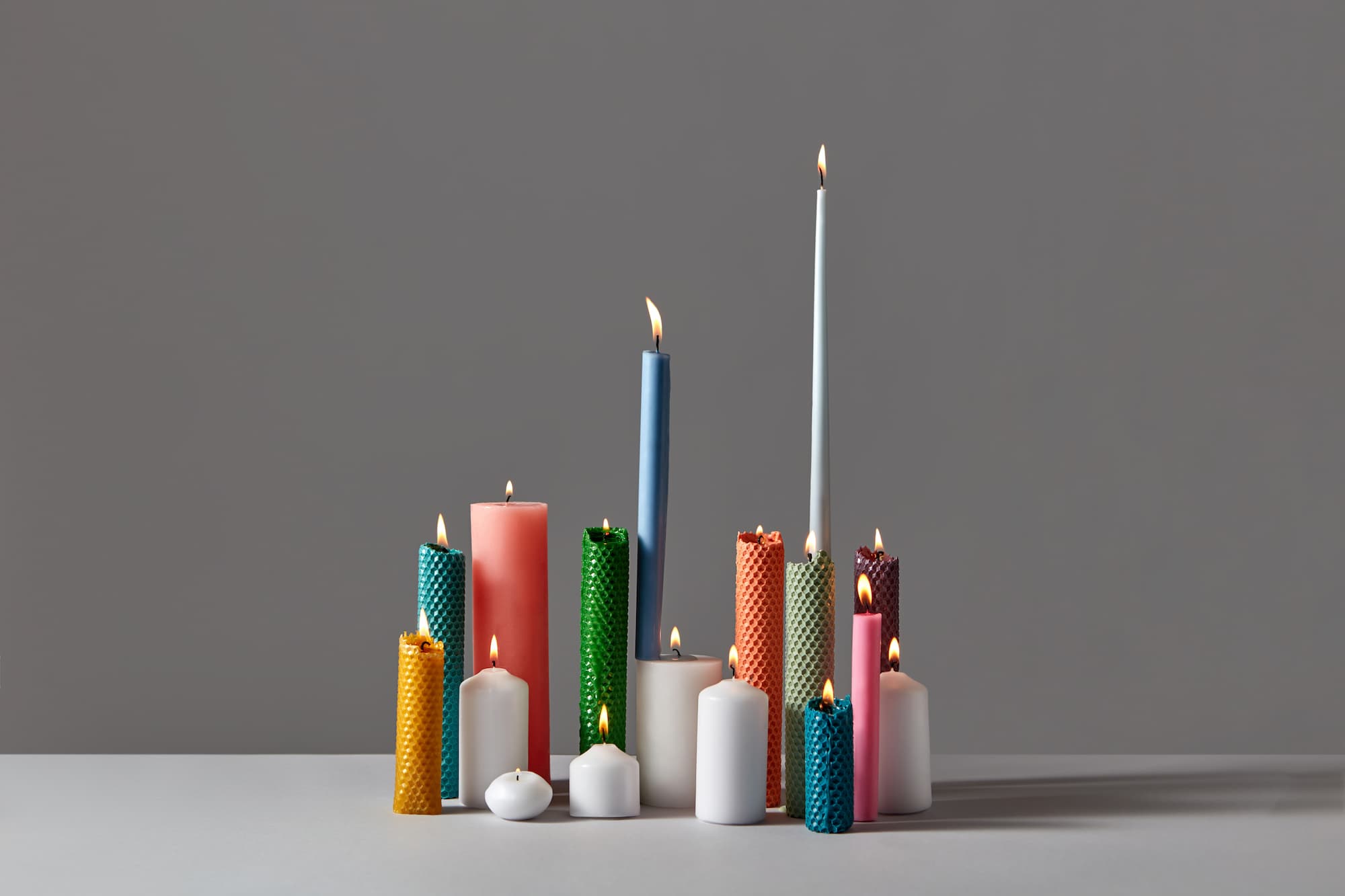 Handmade multi-colored beeswax candles in various shapes on gray background with space for text. Minimal adornment design for Easter or Christmas holiday.