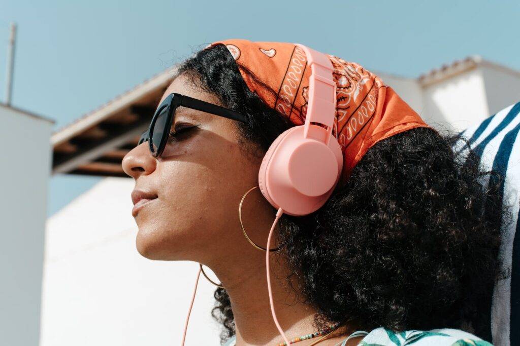Young woman listening to her headphones, wearing a headscarf and sunglasses, during a sunny summer day