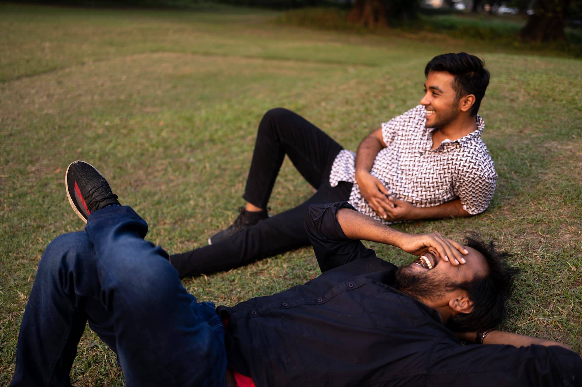 Two Friends Relaxing And Interacting Lying On Grass Ground