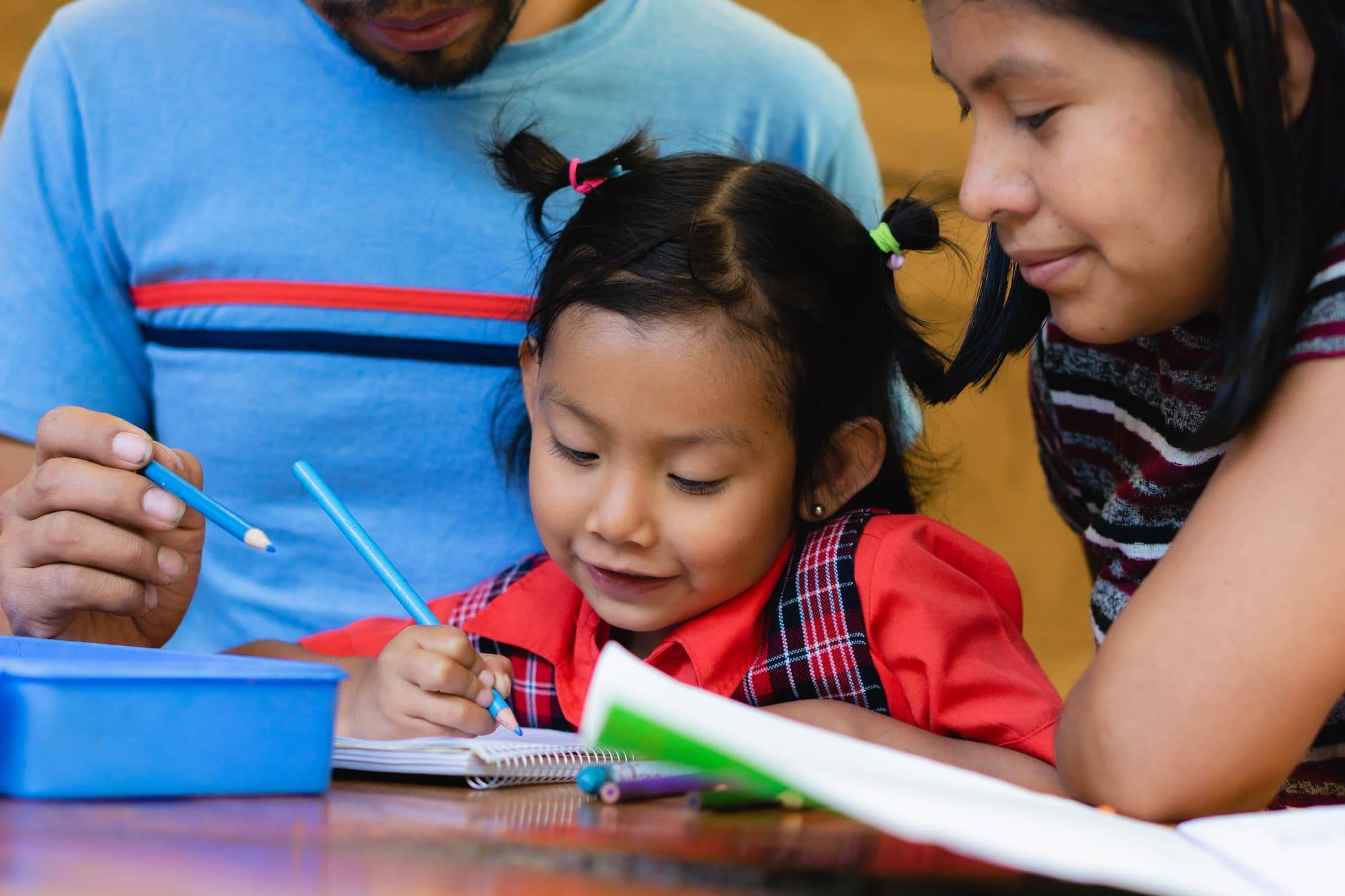 A child practices her writing with parents watching over her.