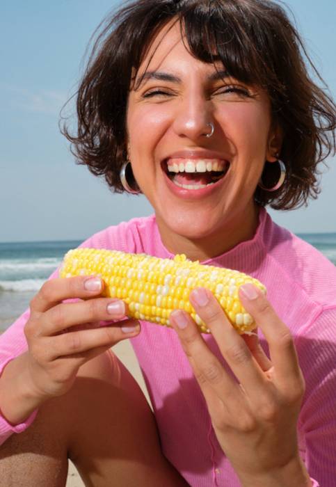 Portrait Of A Young Woman With With Corn On The Beach In Summer