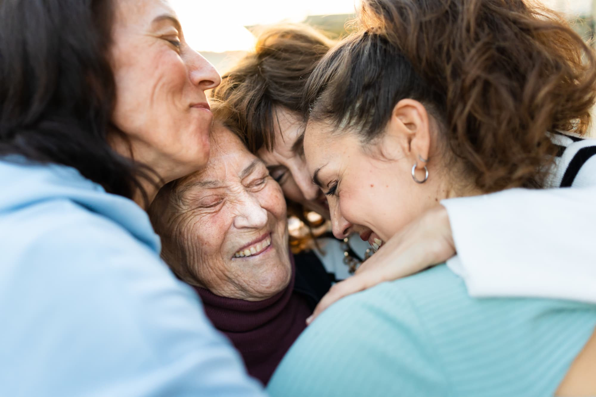 group of women hugging each other, in the center is the grandmother laughing as she receives the love of her family.