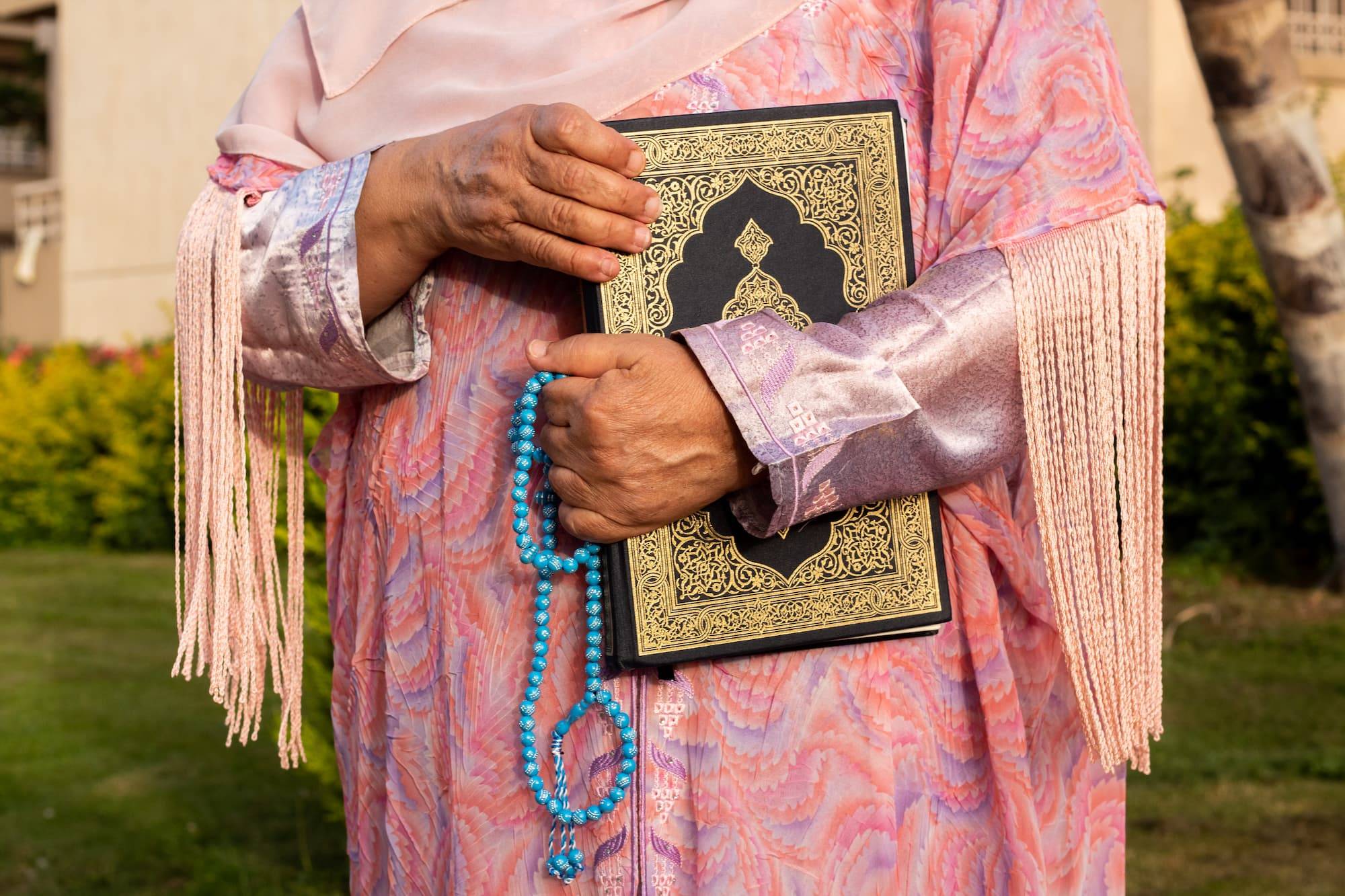 Elderly woman holding Quran and sebha (prayer beads) on Eid while wearing a festive Eid outfit.