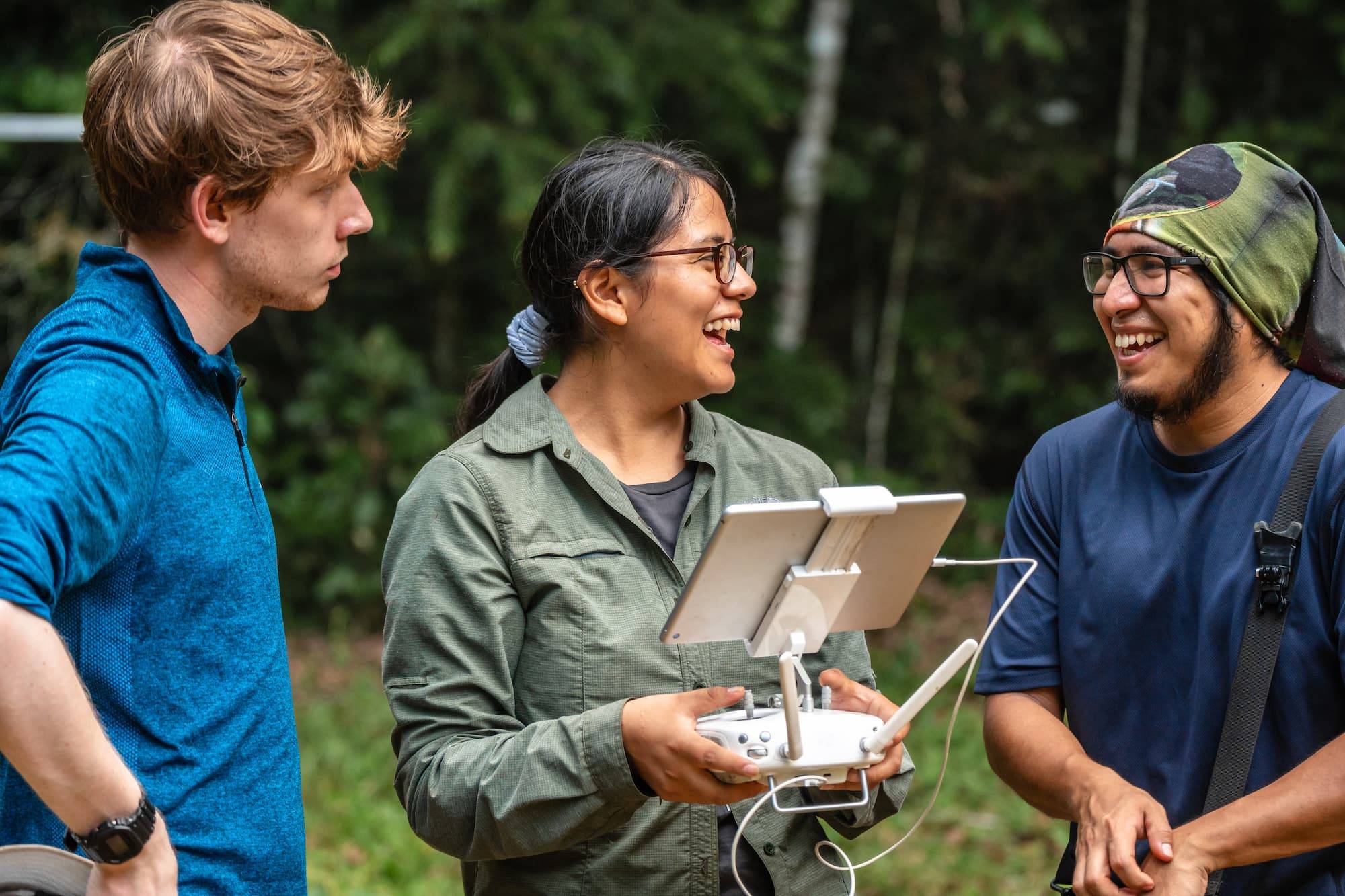 Multi racial group of young people laughing while flying a drone with a tablet controller in a tropical forest. Field biologists doing nature conservation work in the Tambopata National Reserve at the Peruvian Amazon Jungle.