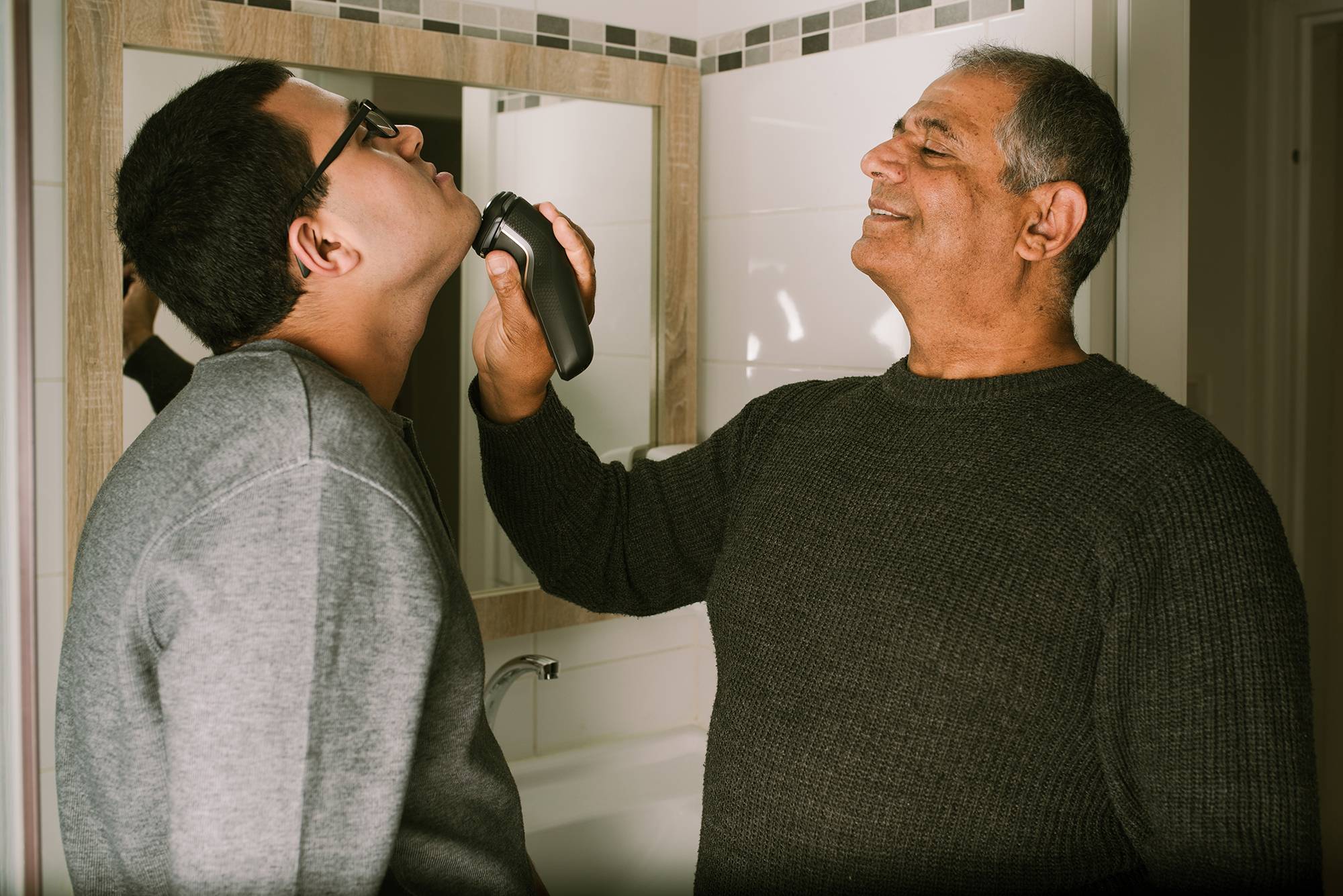 Grandfather Mentors a Teenager, Teaching Him How to Shave with an Electric Razor Near the Bathroom Mirror.