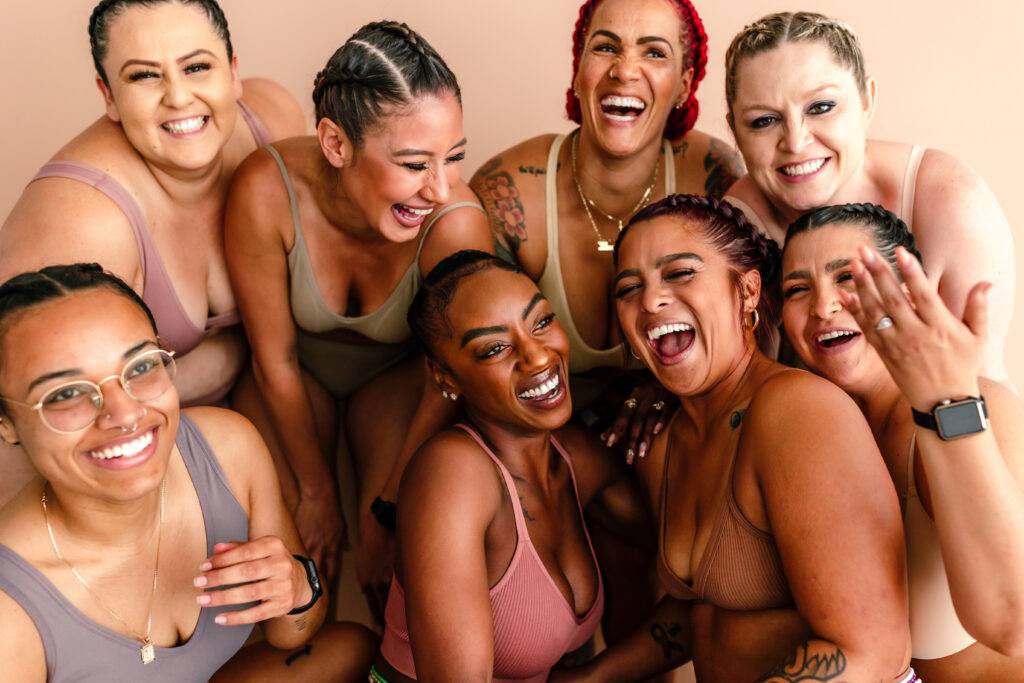 Close up of diverse group of women dressed in bras and panties posing together in studio with neutral backdrop.