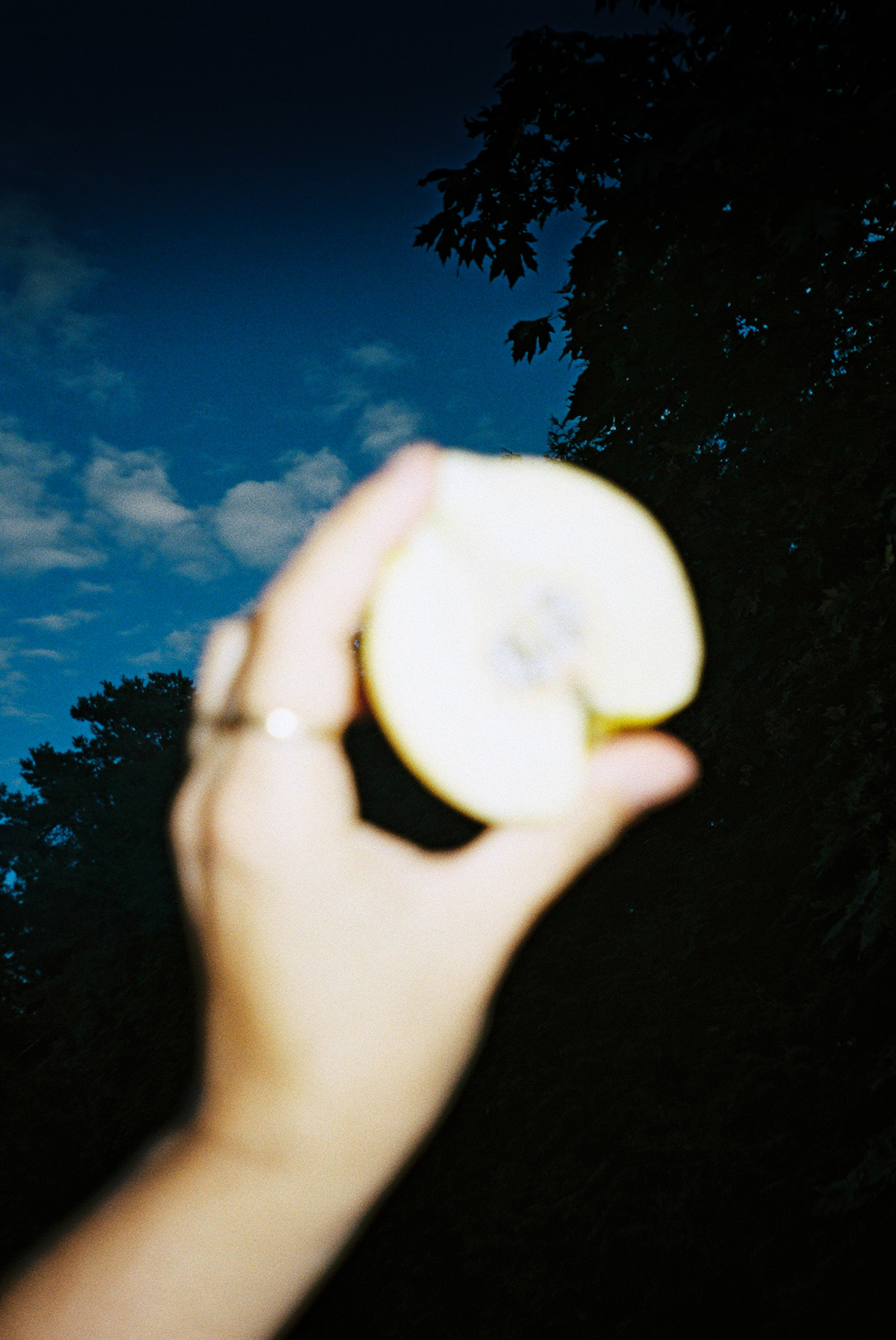 Out of focus hand holding a pear against the sky at dusk. Flash film photography
