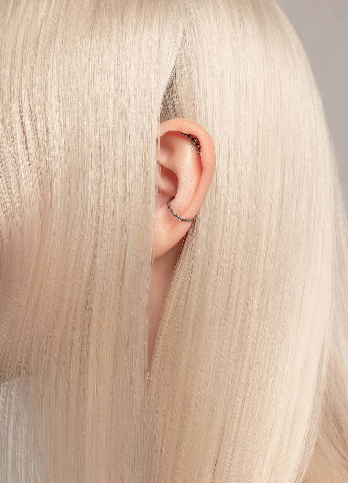 A Close Up Portrait Of An Ear. A close up portrait of an ear with black silver earrings and blond shiny hair around.