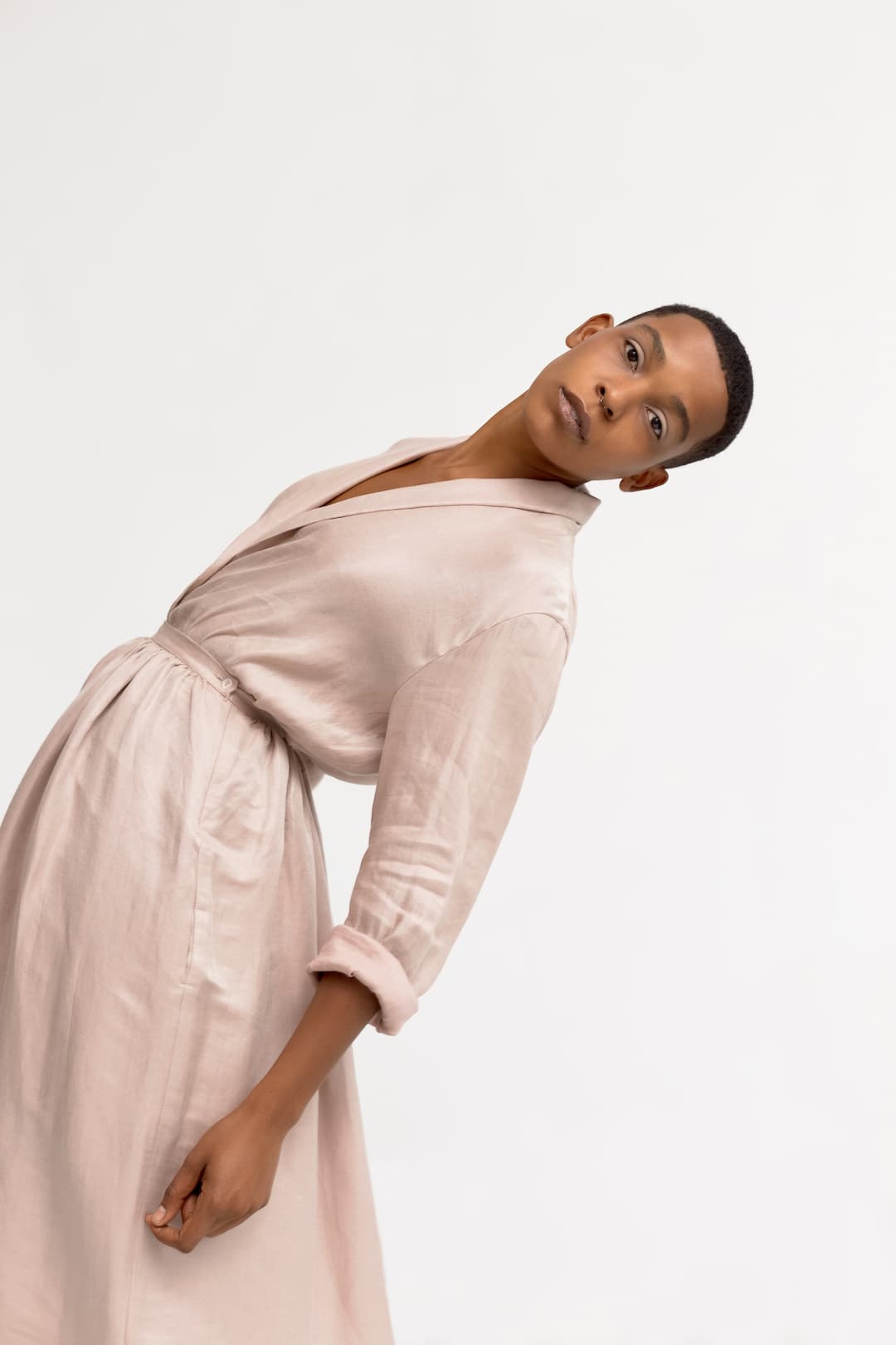 Conceptual portrait of mannish African American woman in silk nightgown bending backward and looking at camera on white background