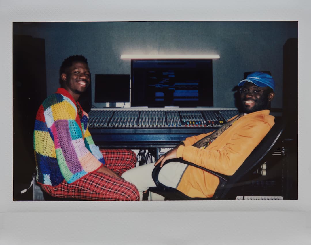 Instant photo of joyful young African American producer and musician sitting in recording studio against mixing console smiling at camera