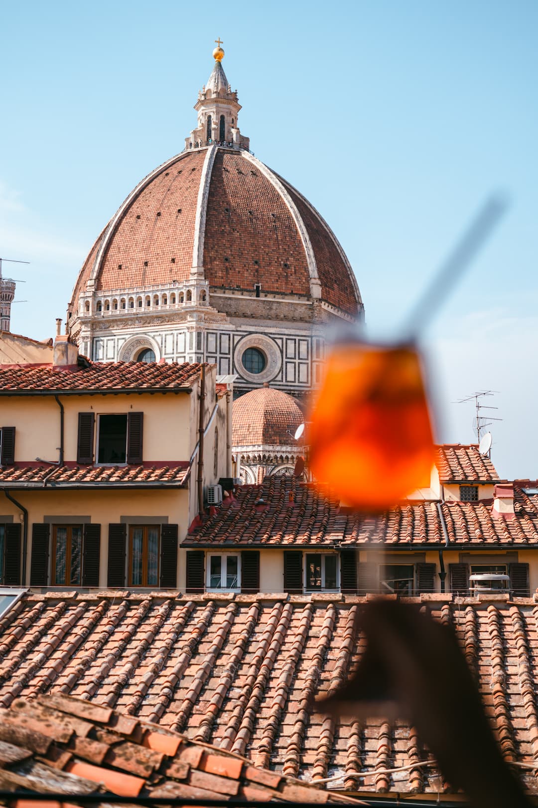 Glass of Aperol Spritz with italian tiled roofs and the Dome of The Cathedral of Santa Maria del Fiore in Florence on baclkground