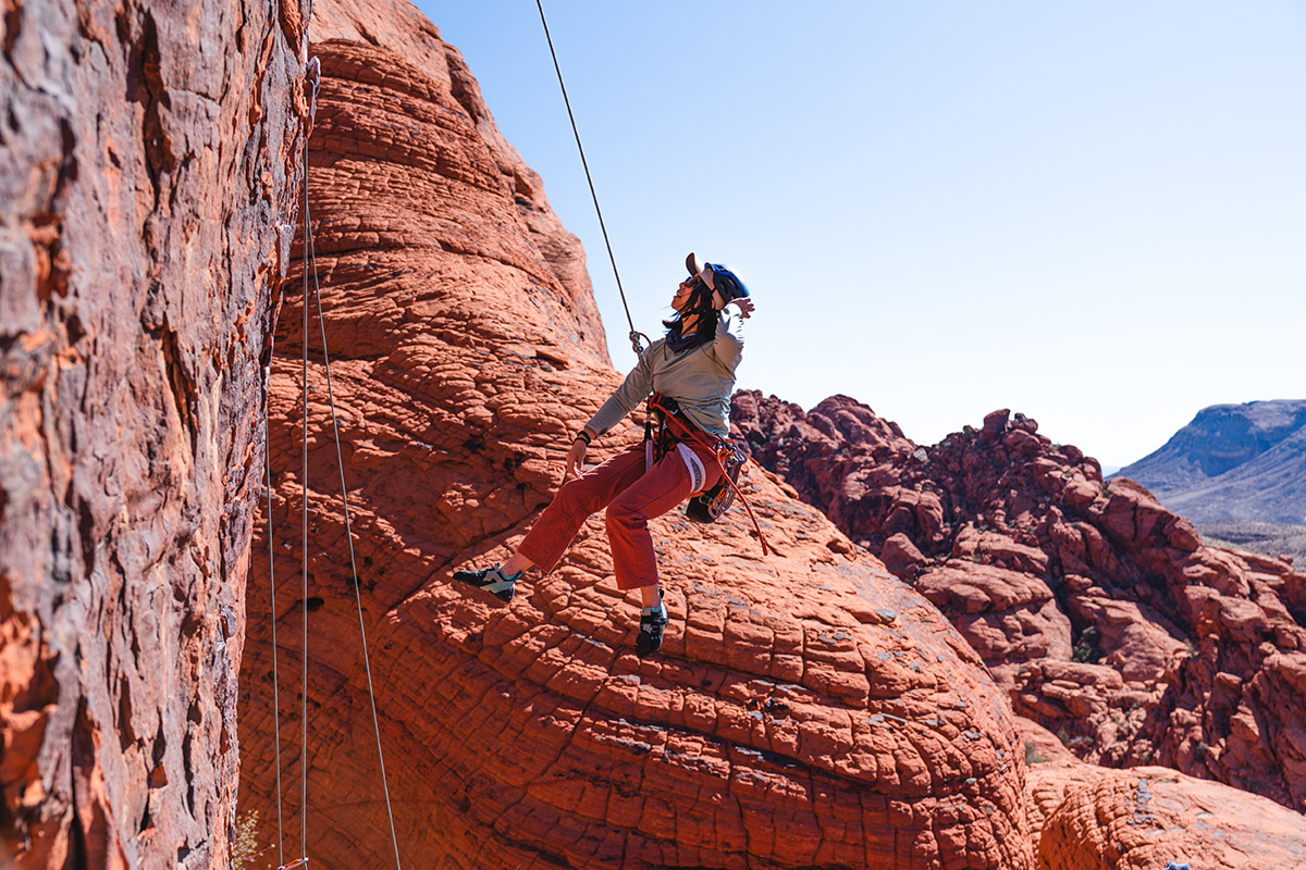 Mai Sawada lead climbing in Red Rock, Nevada. Wearing Sunshade Hoody - Women’s inGypsum Green and Heritage Stand Up Pants in Burl Red. February 6, 2023