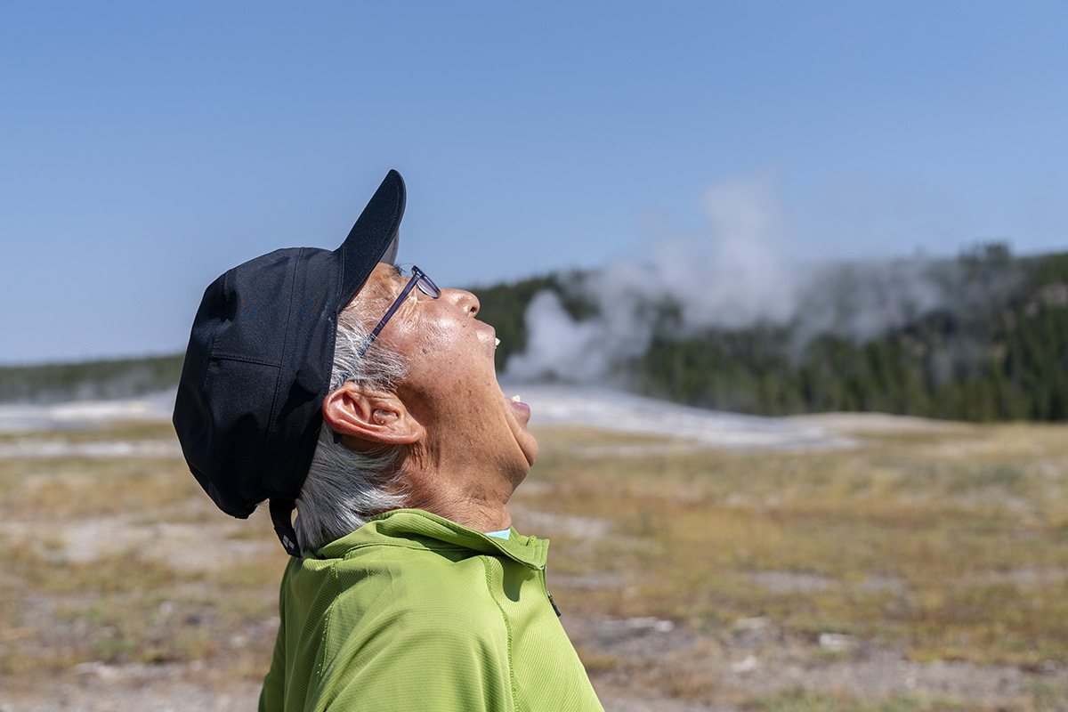 playful tourist having fun old faithful geyser steam pretending to blow smoke yellowstone national park, wyoming, usa,