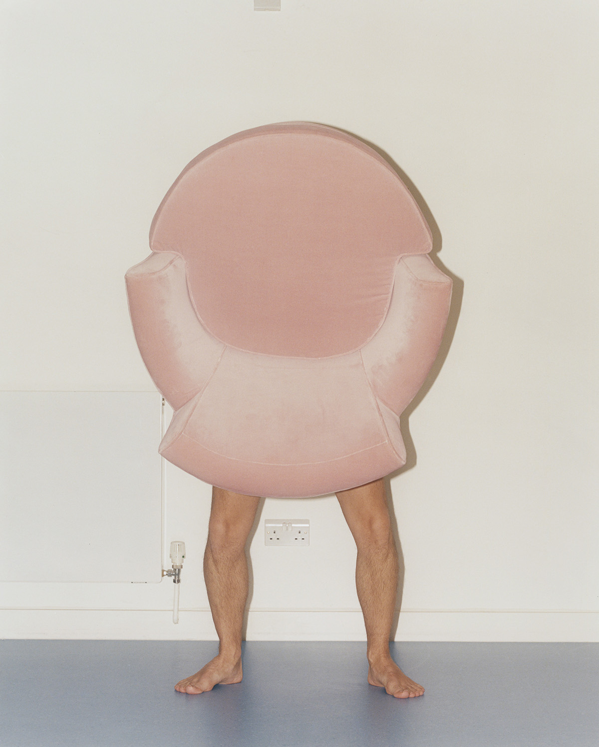 A humorous scene of a person creatively interacting with a pink chair against a minimalist room background, showcasing unique design and playful expression.
