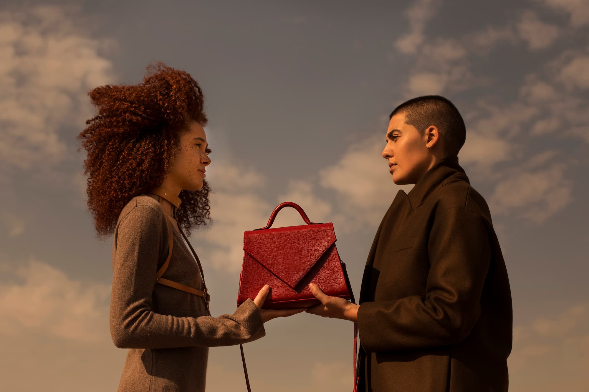 Two different women holding a classic red handbag in the middle of the desert.