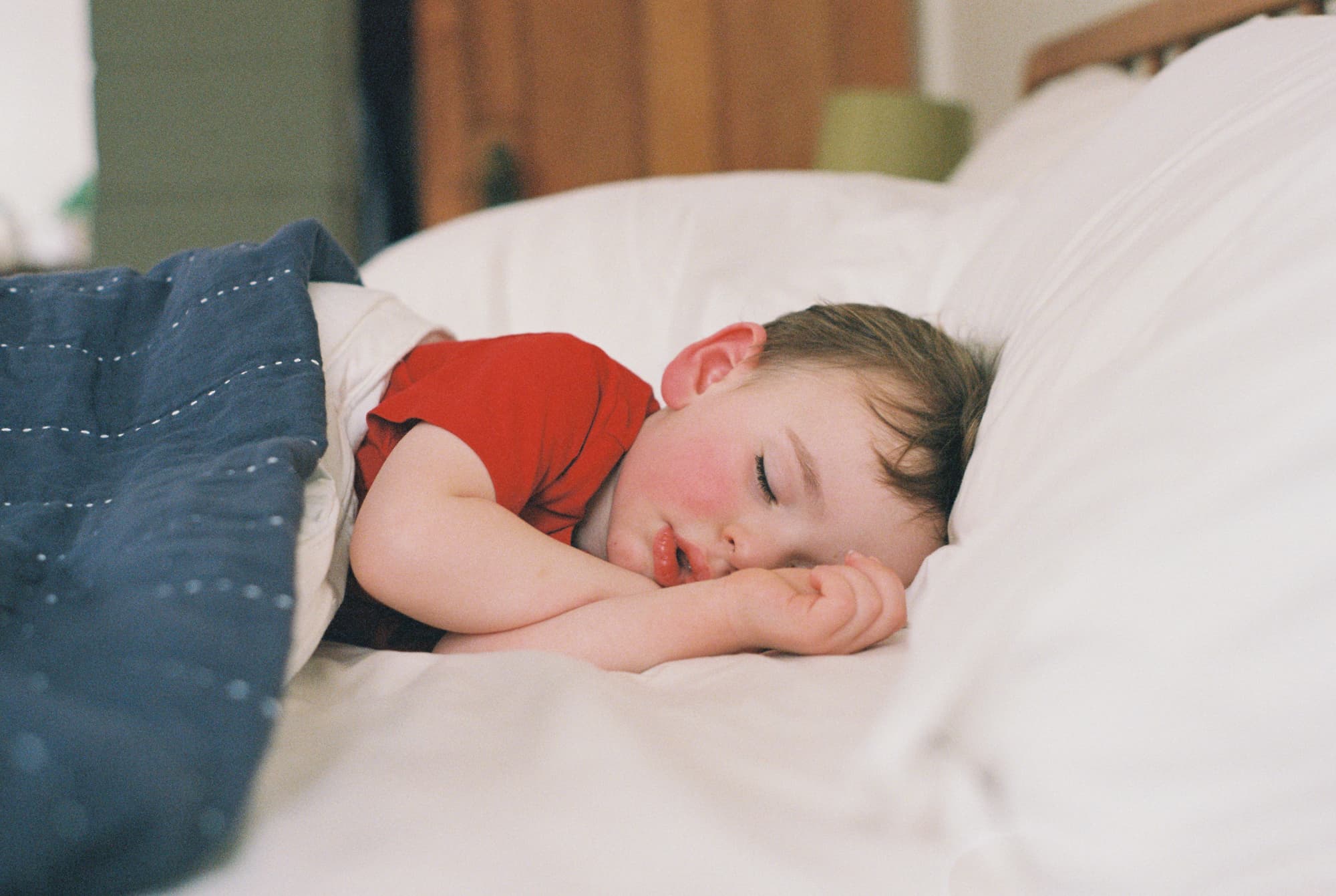 Young child sleeps peacefully in a bed at home. Candid capture on 35mm analog film.