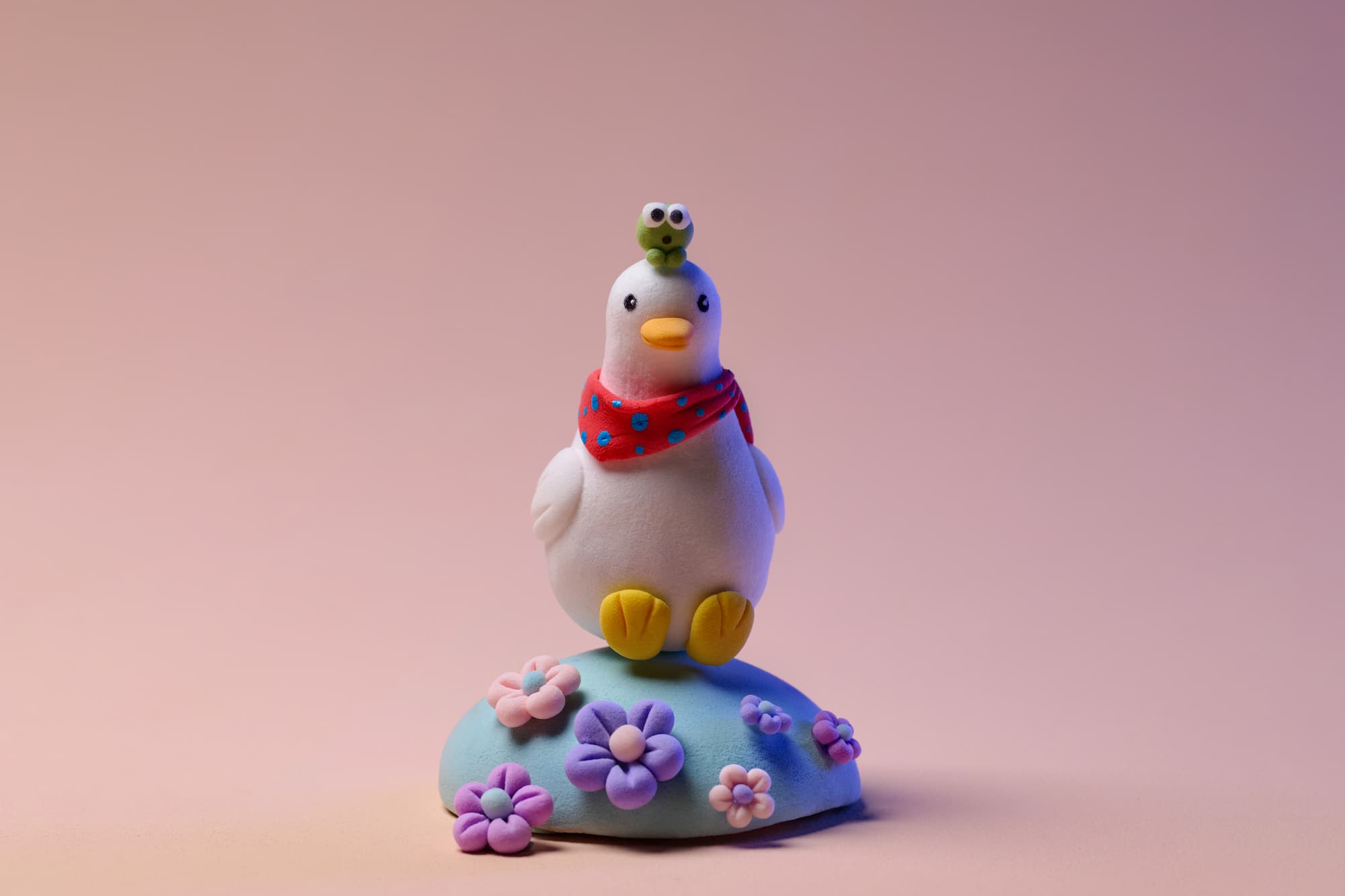 Adorable clay duck figurine with a frog on its head standing on a rock with colorful flowers, set against a peach background.