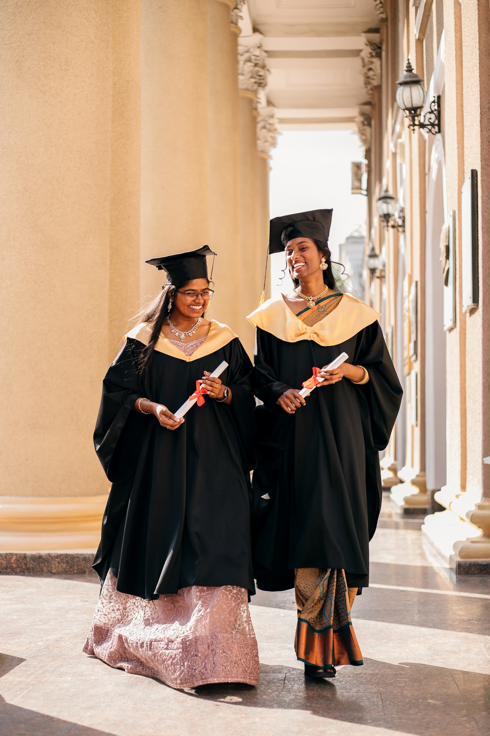 Indian women wearing graduated uniform holding diplomas at university.