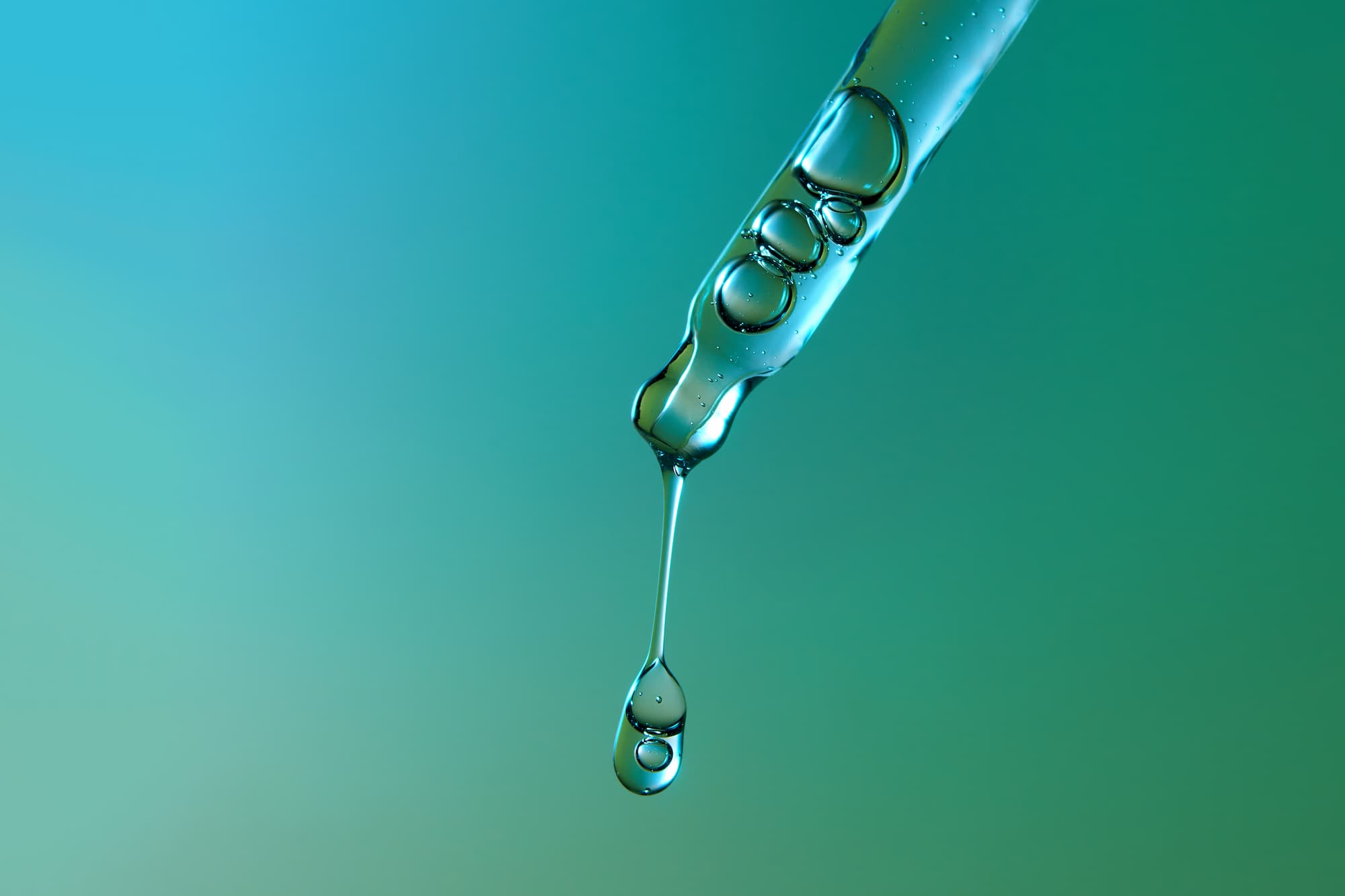 Pipette with large and small bubbles of face serum on gradient emerald green and blue background with droplet falling downwards. Beauty, skincare, anti-age cosmetics