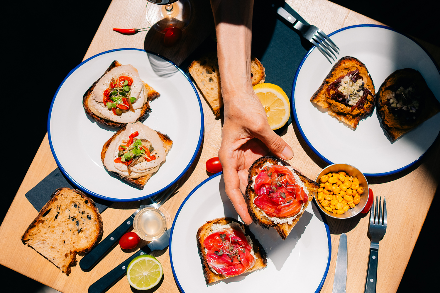 Gourmet Toasts with Various Toppings Delicious gourmet toasts with assorted toppings served on white plates, showcasing a hand picking one up.