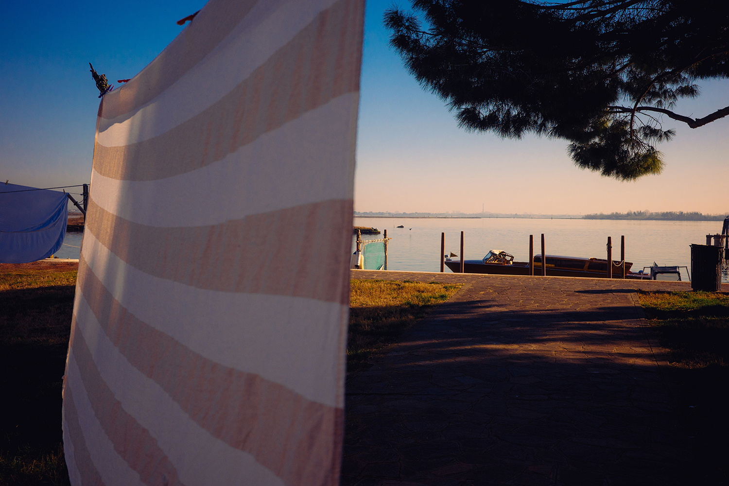 Cloth drying on a line by a lakeside with a boat and peaceful water Striped cloth drying in the breeze near a serene lakeside with a boat docked under a peaceful sunset.