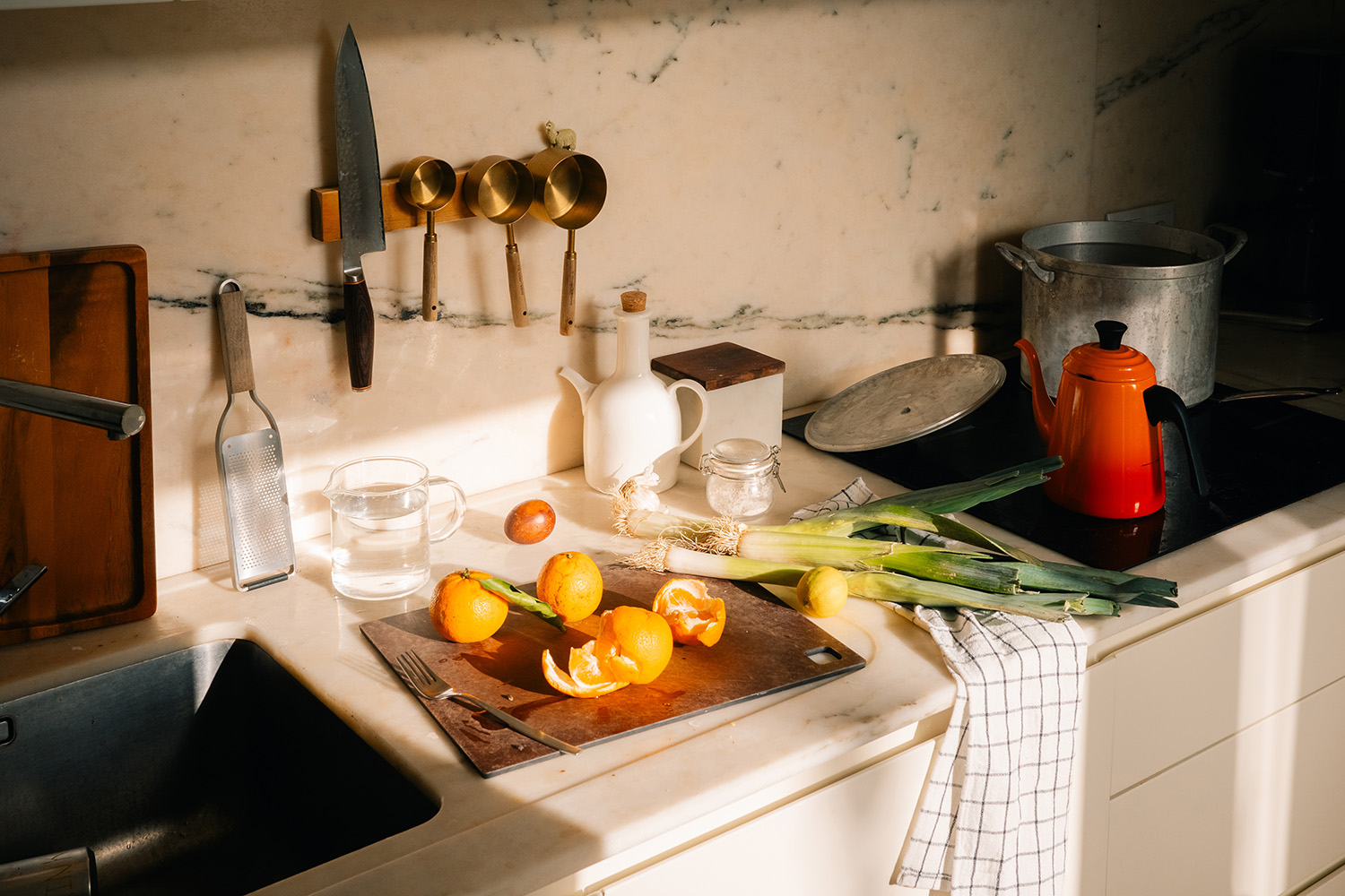 Sunny Kitchen Counter with Fresh Produce and Utensils A warm kitchen scene with fresh oranges, leeks, and utensils in natural light.